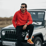 Bold color. Classic ride. Weekend mood. 🔥 Confident man wearing a bright red hoodie, black pants, and yellow-red sneakers sitting on a white Jeep outdoors, showcasing urban streetwear and adventure style