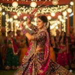 Young woman in vibrant pink and multicolor traditional lehenga dancing Garba with decorated dandiya sticks under festive lights during Navratri celebrationHer vibrant attire, intricate jewelry, and graceful movements showcase the rich artistry of Gujarati culture, making the scene perfect for festival promotions, fashion features, cultural heritage blogs, social media campaigns, and travel or event marketing. The photo radiates festive excitement, traditional music, and community celebration, ideal for SEO around Navratri dance nights, Indian folk art, and ethnic fashion inspiration.