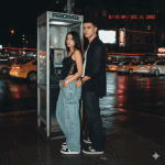 Stylish young couple in Y2K streetwear posing by a vintage payphone on a rainy city street at night with neon lights and moving traffic