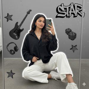 Ultra-realistic 8K cinematic portrait of a stylish young woman sitting casually on the floor, taking a mirror selfie. She wears a loose black shirt and white pants, holding her shirt with one hand and the phone with the other. Minimal jewelry, relaxed expression, soft natural light, and a white outline glow. The background features a modern grayscale collage with an electric guitar, headphones, dice, cat face decor, 3D stars, and “STAR” graffiti text.