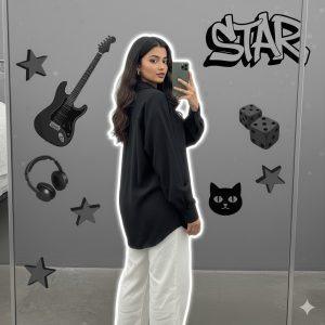 Ultra-detailed 8K cinematic Instagram-style portrait of a stylish young woman standing with her back slightly turned toward a mirror, looking over her shoulder at the camera. She wears a loose black shirt and white pants with minimal jewelry, holding her phone casually. Realistic lighting, soft white outline glow, and grayscale background collage featuring an electric guitar, headphones, dice, cat face decor, metallic stars, and “STAR” graffiti text.
