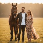 "A stylish young couple posing with a majestic horse in an open field during golden hour. The man wears a leather jacket and jeans, the woman a flowing modern maxi dress. Both face the camera smiling, with soft cinematic lighting and ultra-realistic textures."