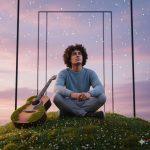 A young man with curly hair in a light blue sweater and gray pants sits on a lush moss-covered hill, surrounded by small white and orange flowers. He gazes thoughtfully at a dreamy pink and purple sky with sparkling stars. An acoustic guitar, partially covered in moss, stands beside him. Abstract black geometric frames extend into the sky, creating a surreal, tranquil scene with cinematic lighting and photorealistic textures.